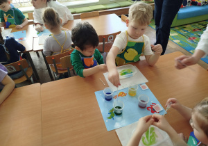 Dzieci siedzą przy stolikach i wykonują eksperyment z mlekiem, barwnikiem i płynem do mycia naczyń