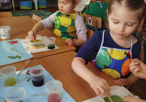 Dwie dziewczynki siedzą przy stoliku i wykonują doświadczenie z mlekiem, barwnikiem i płynem do mycia naczyń