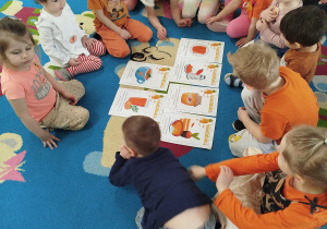 Grupa dzieci na dywanie ogląda ilustracje przedstawiające wartości odżywcze marchewki