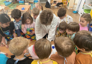 Grupa dzieci i studentka zgromadzeni wokół ławki