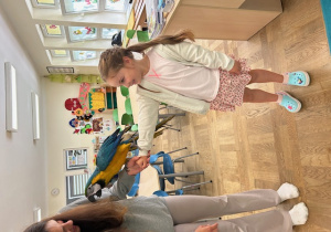 Edukatorka z dziewczynką na ręce, której stoi papuga