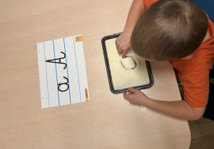 chłopiec rysuje po kaszy mannej