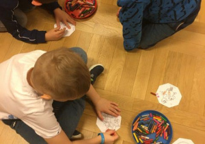 dzieci siedzą na podłodze i kolorują obrazki